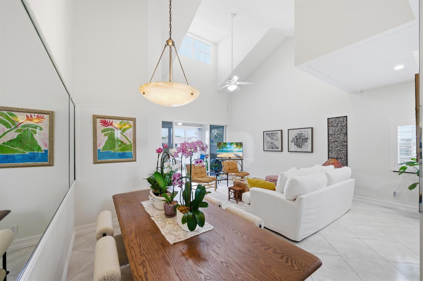 A dining area with a wooden table leads into a living room with vaulted ceilings — 47 N Lakeshore Drive, Hypoluxo FL 33462, HYPOLUXO, FL