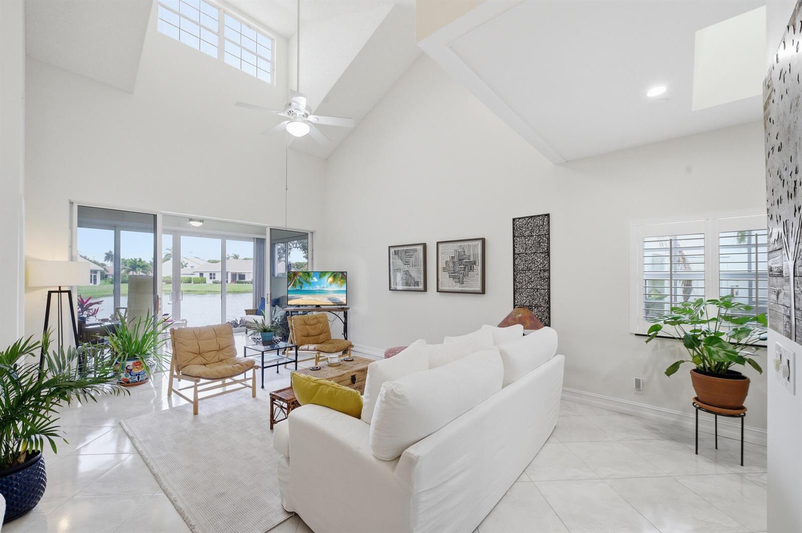 A bright living room features vaulted ceilings, white tile floors, and sliding doors to a lake — 47 N Lakeshore Drive, Hypoluxo FL 33462, HYPOLUXO, FL