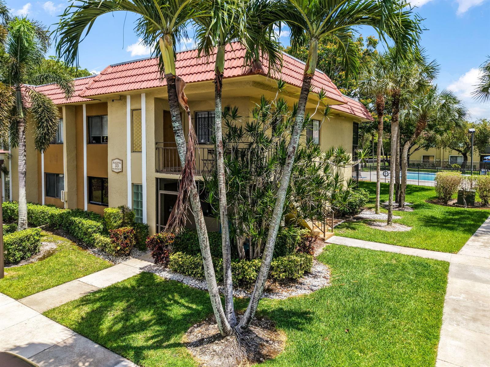 A two-story apartment building with a red tile roof surrounded by palm trees and landscaping — 303 Lakeview Drive # 102, Weston FL 33326, WESTON, FL