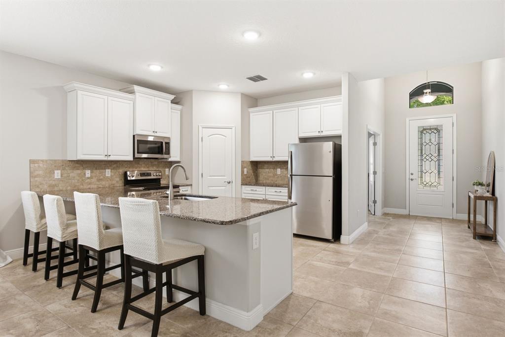 A kitchen features white cabinetry, granite countertops, stainless steel appliances, and a breakfast bar island — 11392 WEAVER HOLLOW ROAD, NEW PORT RICHEY, FL