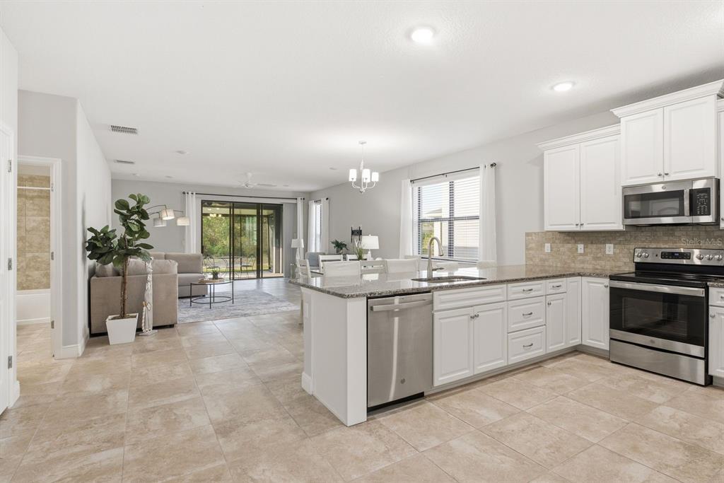 A kitchen with white cabinets and stainless steel appliances opens into a living room area — 11392 WEAVER HOLLOW ROAD, NEW PORT RICHEY, FL