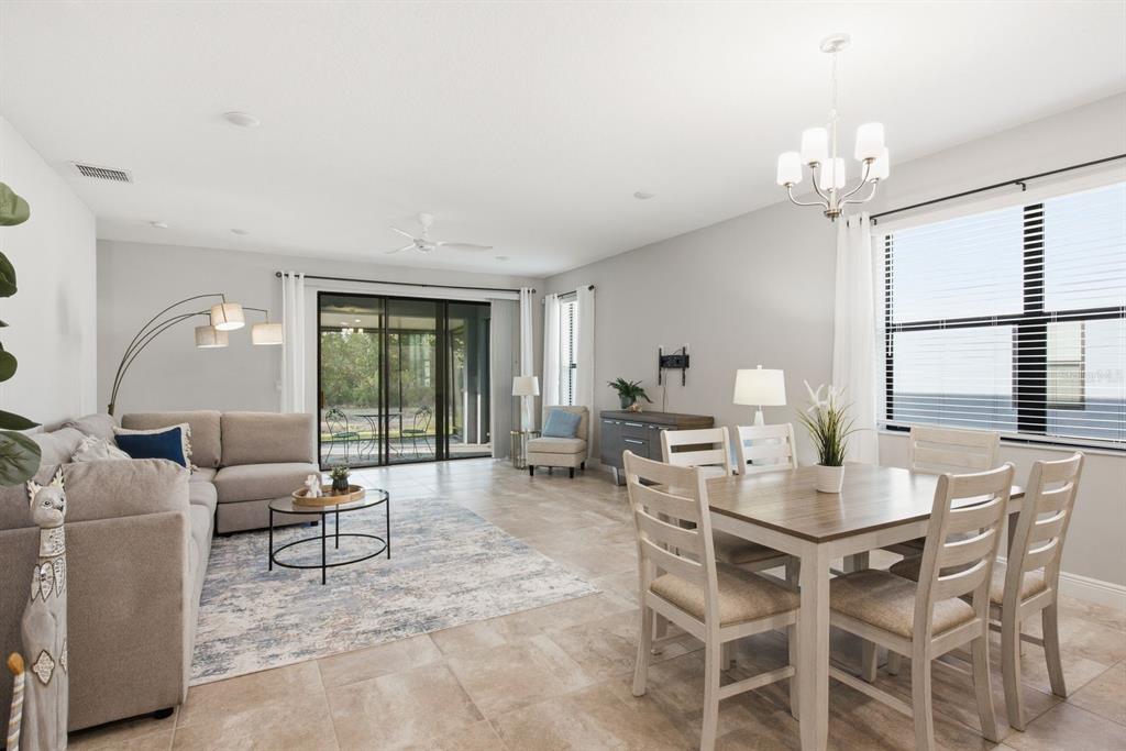 An open-concept living and dining area features tile flooring, a sectional sofa, and sliding doors — 11392 WEAVER HOLLOW ROAD, NEW PORT RICHEY, FL
