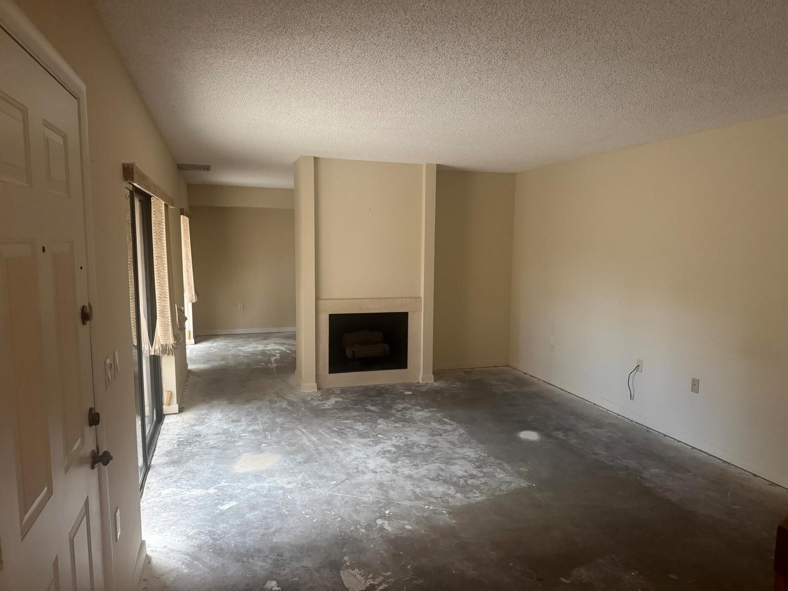 An empty living room features a central fireplace, beige walls, and unfinished concrete flooring — 219 2nd Lane, Palm Beach Gardens FL 33418, PALM BEACH GARDENS, FL