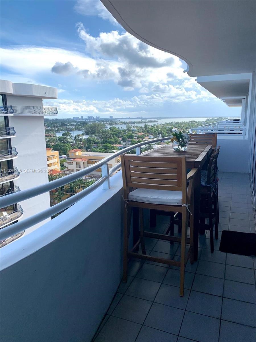 A balcony features a wooden dining set overlooking a coastal city and waterway — 8911 Collins Ave # 1104, Surfside FL 33154, SURFSIDE, FL