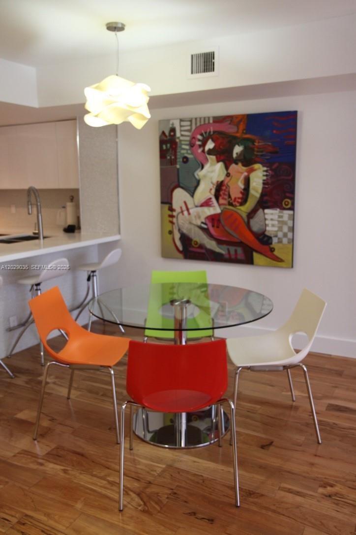 A dining area features a glass table with colorful chairs beneath a modern pendant light — 8911 Collins Ave # 1104, Surfside FL 33154, SURFSIDE, FL