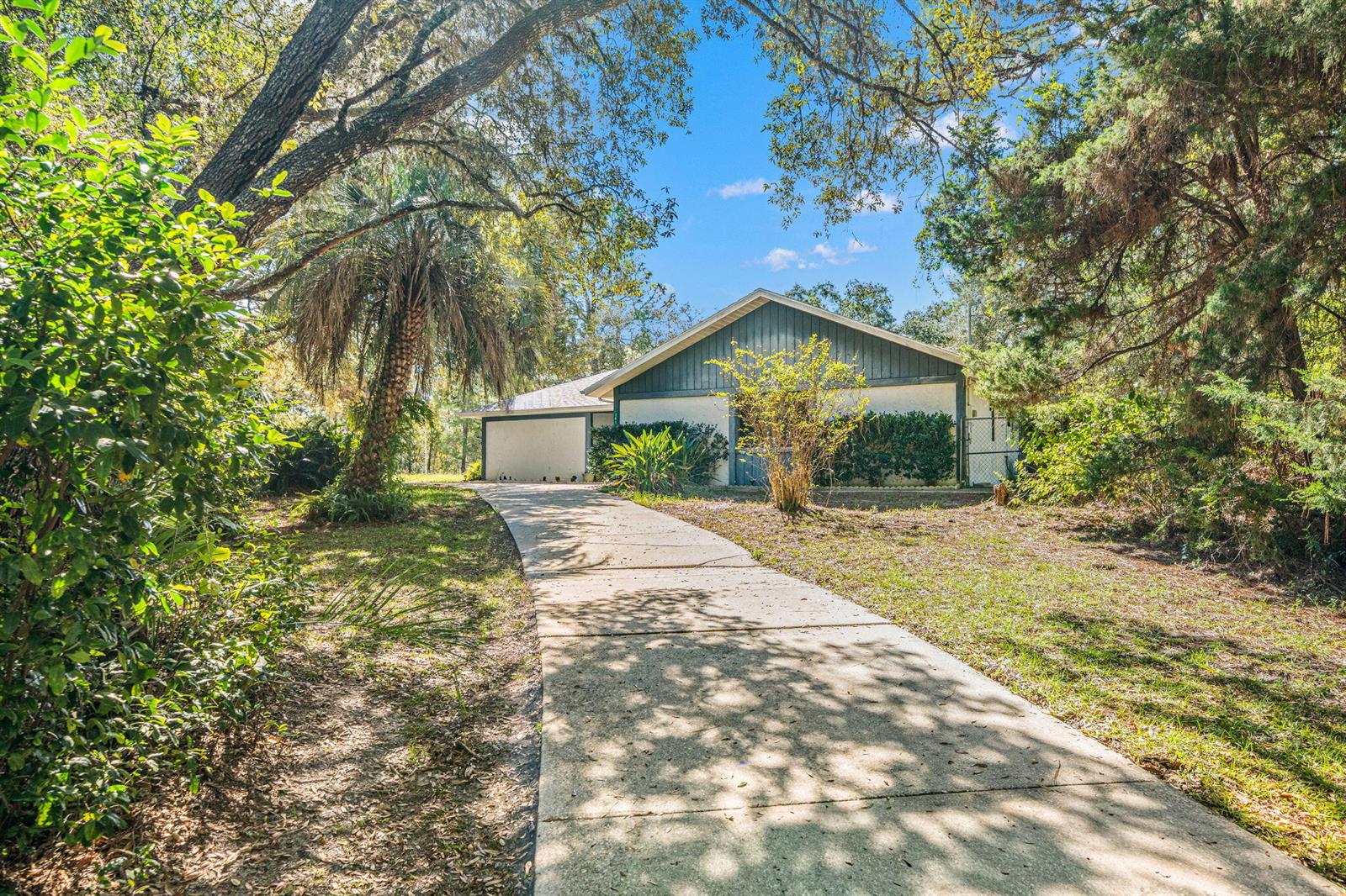 A concrete driveway leads to a single-story house surrounded by trees and landscaping — 7418 N Firwood Circle, FL 34433, FL