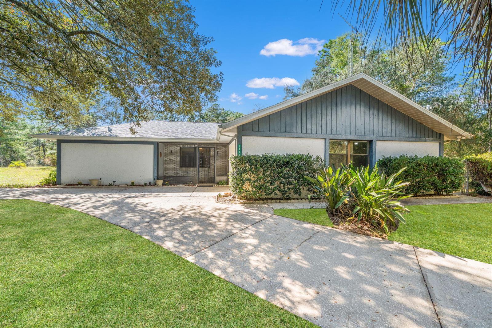 A single-story house with a concrete driveway, white stucco walls, and gray vertical siding — 7418 N Firwood Circle, FL 34433, FL