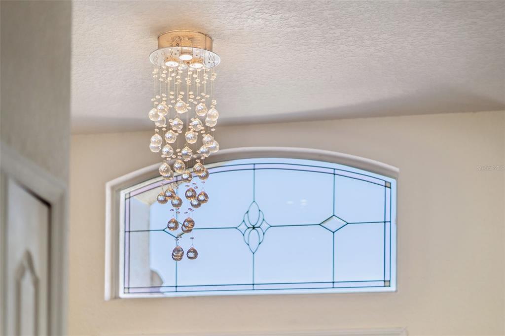 A crystal chandelier hangs from the ceiling in front of an arched stained-glass window — 722 BIRKDALE STREET, DAVENPORT, FL
