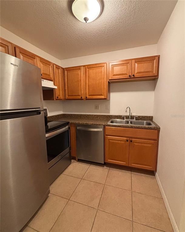 A kitchen features wood cabinets, stainless steel appliances, a double sink, and tiled flooring — 6519 W NEWBERRY ROAD UNIT 604, GAINESVILLE, FL
