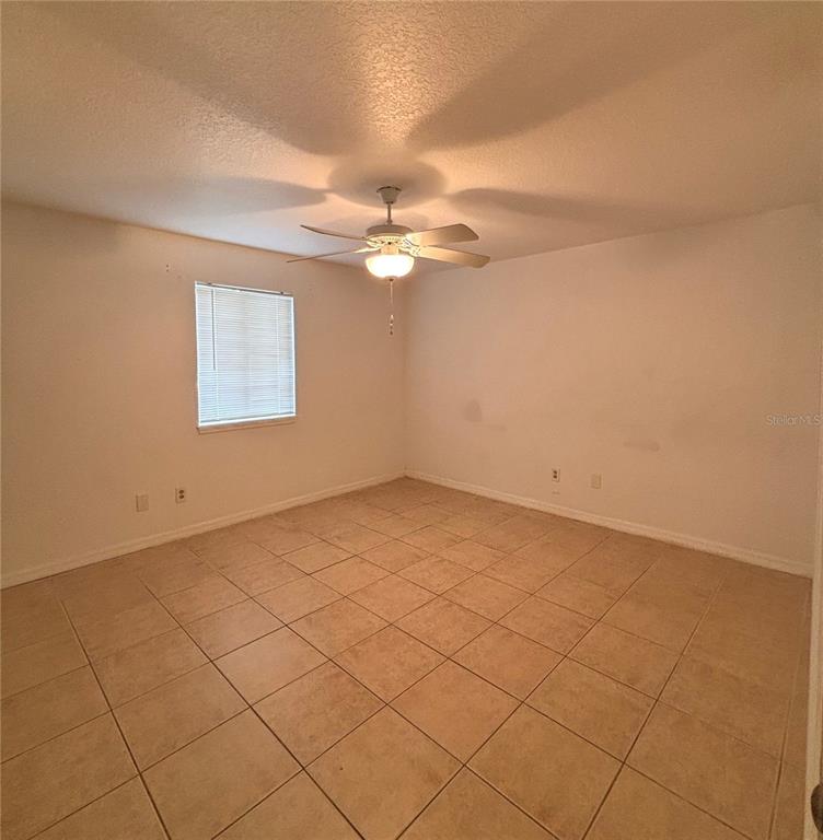 An empty room features beige tile flooring, white walls, and a ceiling fan — 6519 W NEWBERRY ROAD UNIT 604, GAINESVILLE, FL