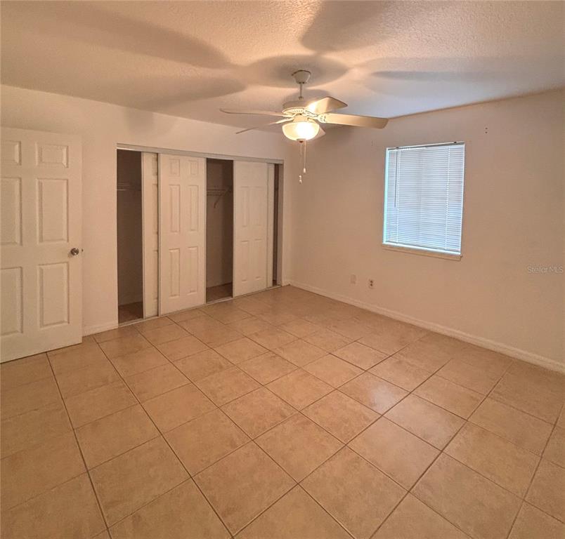 A bedroom with beige tile flooring, a ceiling fan, a window, and sliding closet doors — 6519 W NEWBERRY ROAD UNIT 604, GAINESVILLE, FL