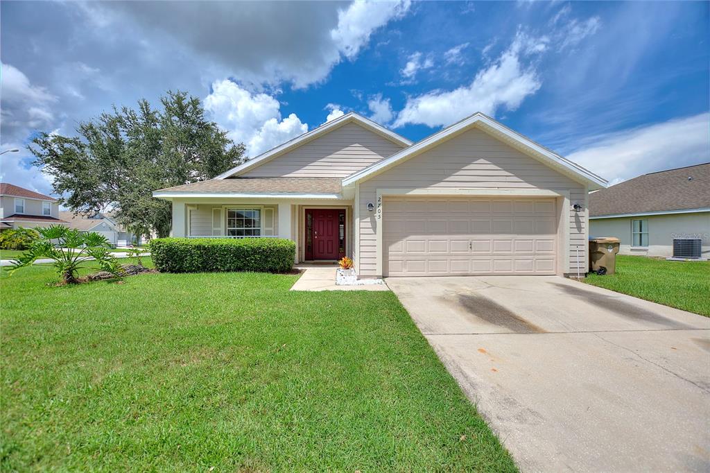 A single-story house with beige siding, a red front door, and a two-car garage — 2705 PRESTWICK LANE, KISSIMMEE, FL