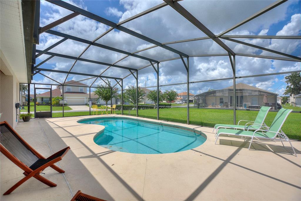A screened-in patio features a kidney-shaped swimming pool and lounge chairs on a concrete deck — 2705 PRESTWICK LANE, KISSIMMEE, FL