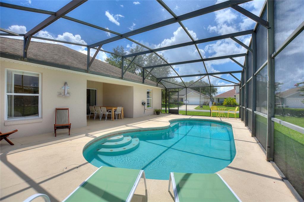 A screened-in pool patio features a kidney-shaped pool, lounge chairs, and a covered dining area — 2705 PRESTWICK LANE, KISSIMMEE, FL