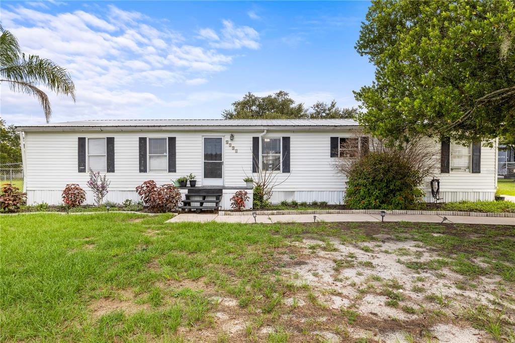 A single-story white mobile home features black shutters, a metal roof, and a front porch — 4332 UPPER MEADOW ROAD, MULBERRY, FL
