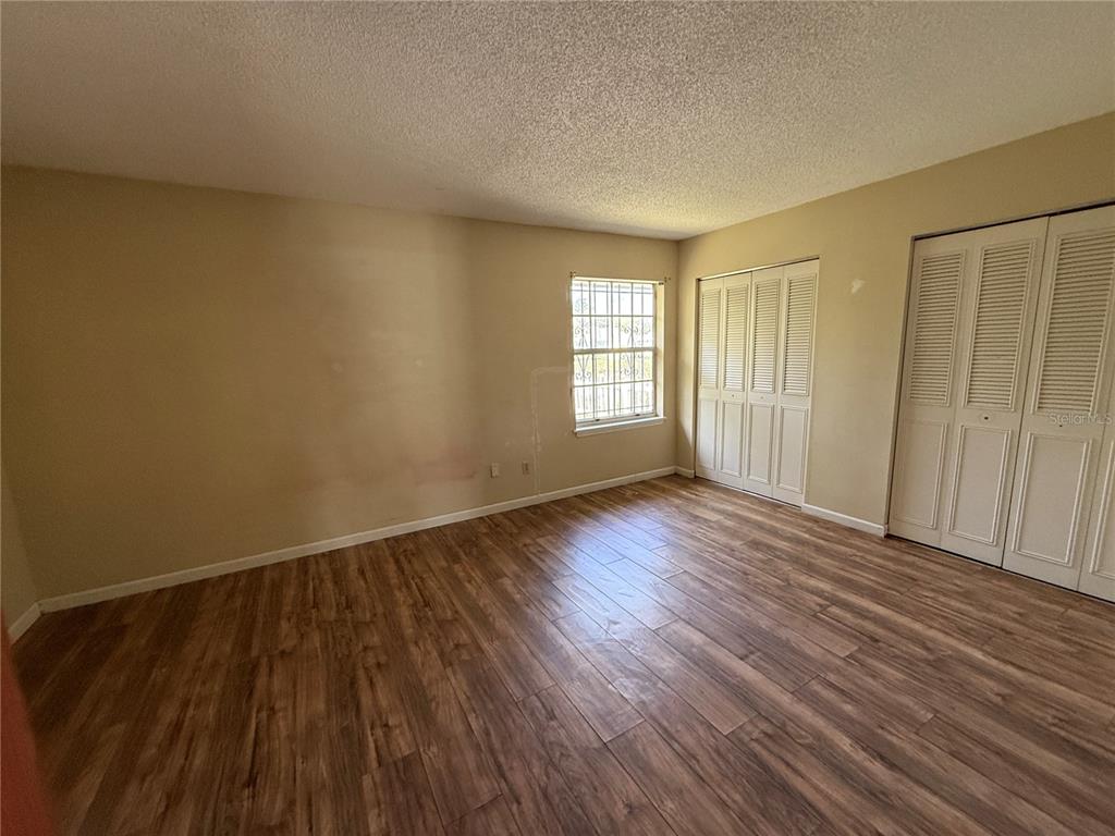 An empty bedroom features light-colored walls, wood-look flooring, a window with security bars, and closets — 22 BIRDIE DRIVE, NEW SMYRNA BEACH, FL