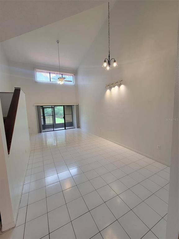 A bright, high-ceilinged room features white tile flooring, a chandelier, and a sliding glass door — 3333 GRAY FOX COVE UNIT 3333, APOPKA, FL