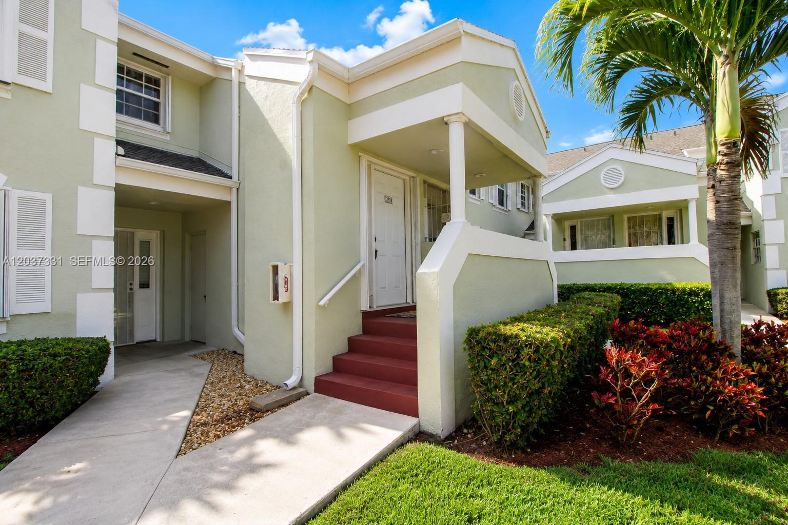A light green two-story townhouse exterior features a covered entrance with red stairs — 2518 SE 20th Pl # B, Homestead FL 33035, HOMESTEAD, FL