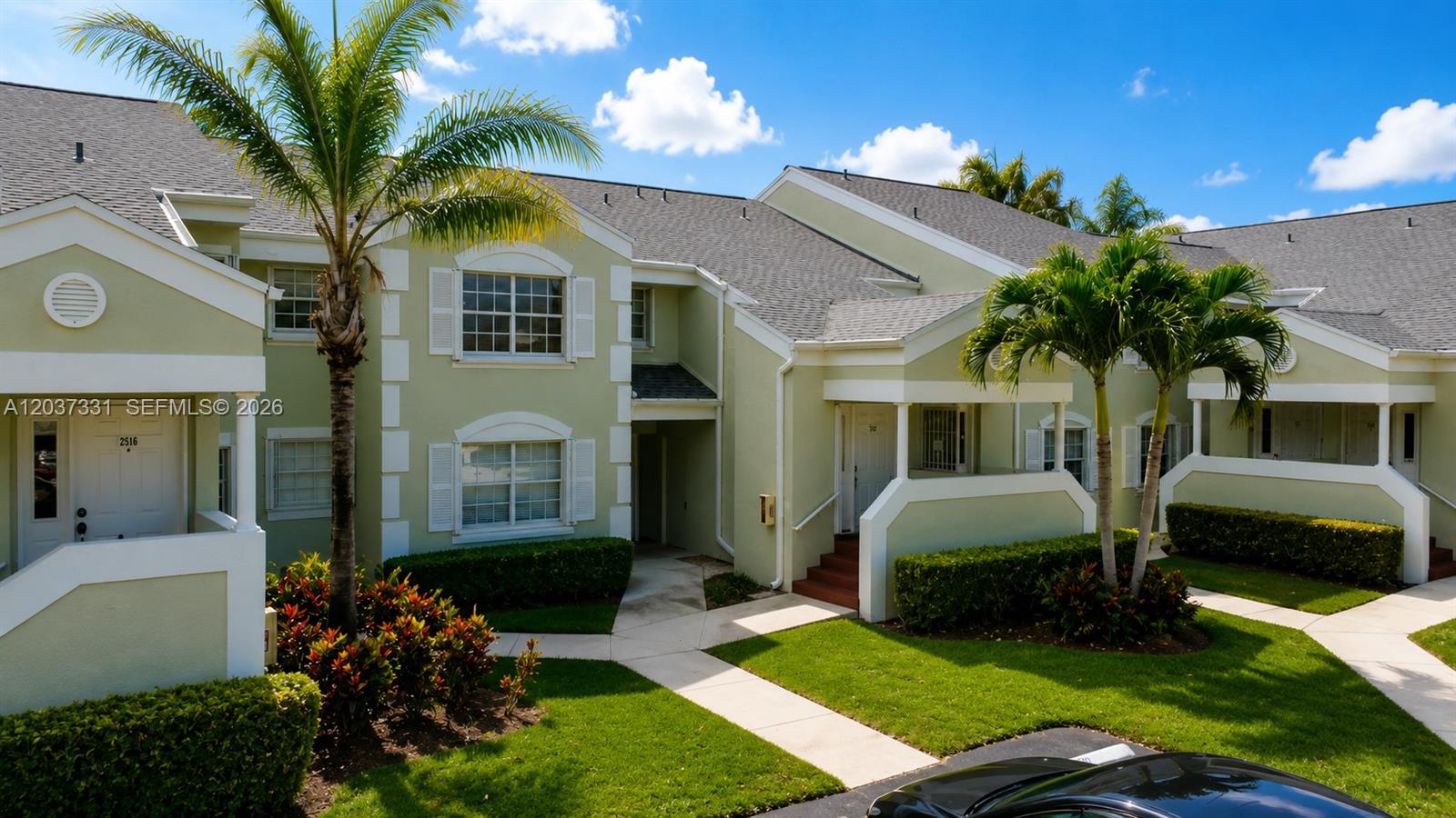 A two-story light green apartment building features white trim, palm trees, and a paved walkway — 2518 SE 20th Pl # B, Homestead FL 33035, HOMESTEAD, FL