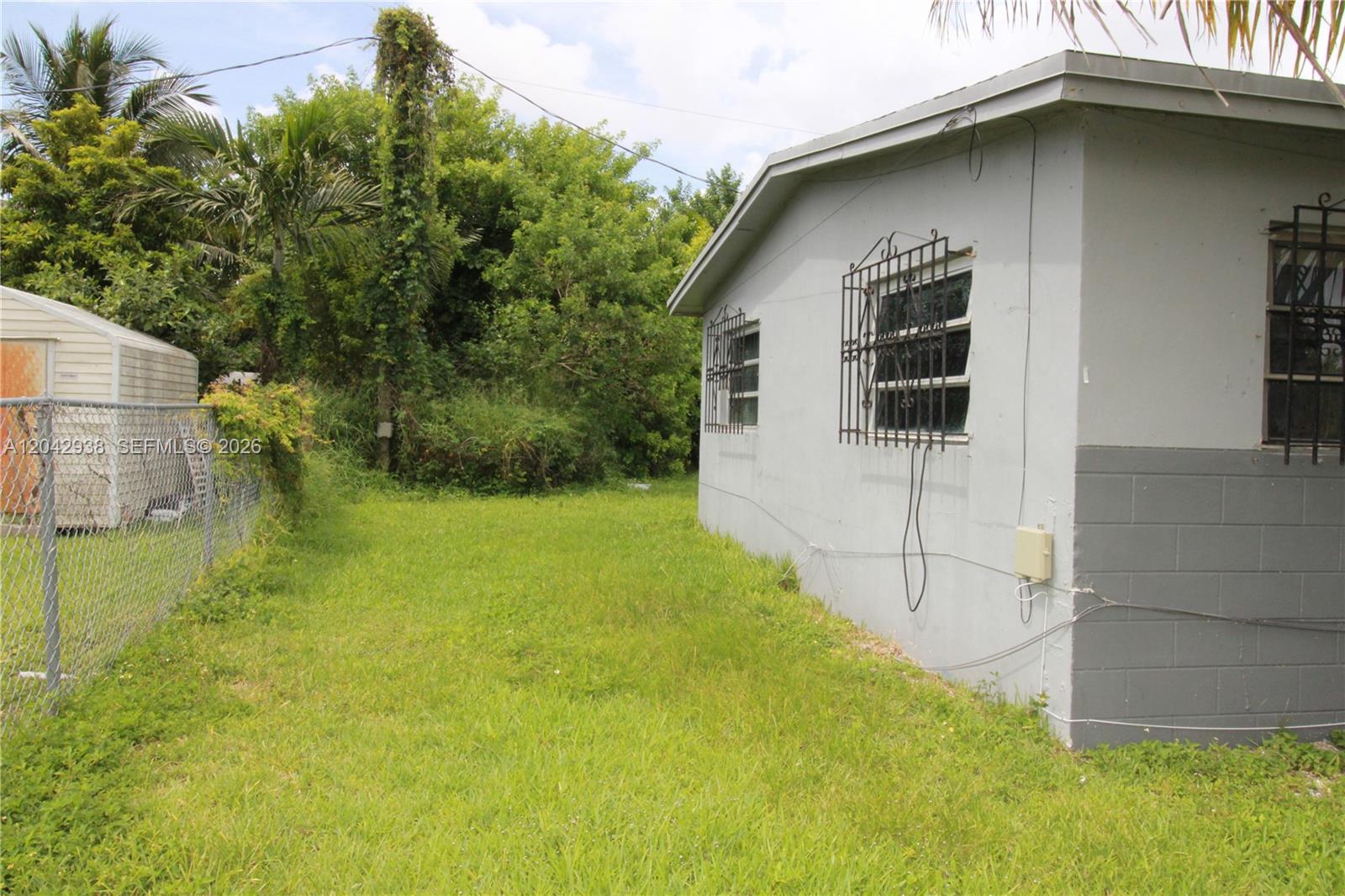 A side view of a gray house exterior with window security bars and a grassy yard — 10820 SW 220th St, Miami FL 33170, MIAMI, FL