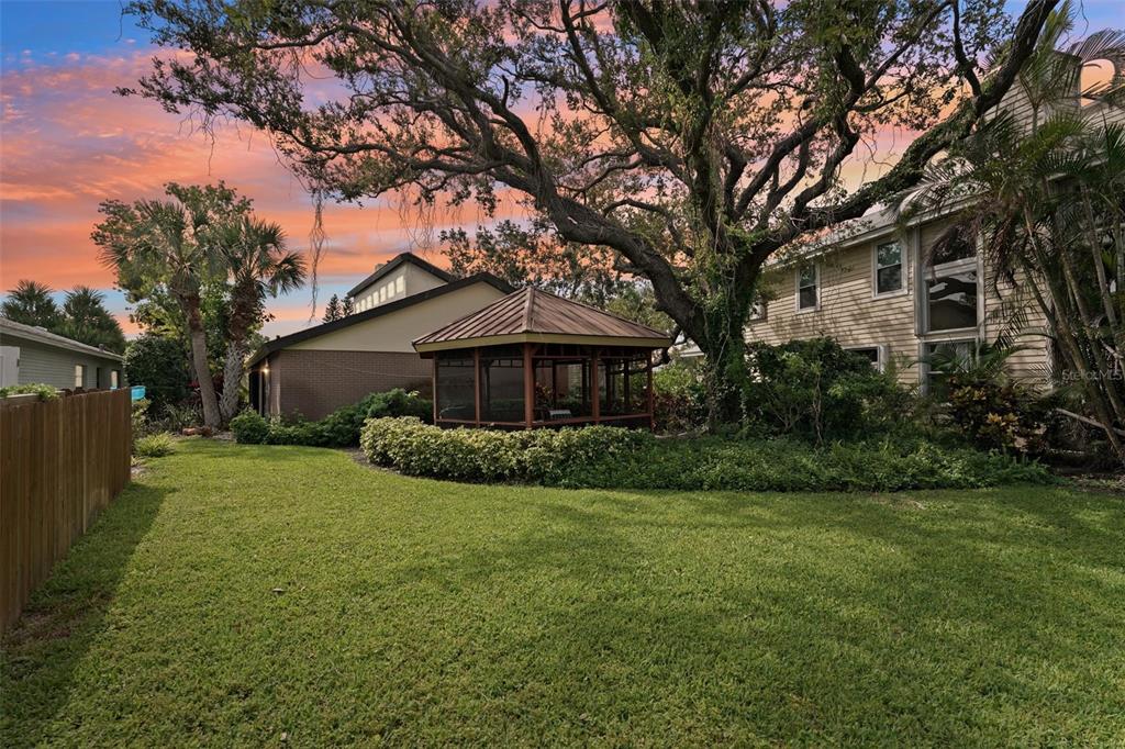 A backyard features a screened gazebo, a large tree, and a two-story house at sunset — 2312 89TH STREET NW UNIT 32, BRADENTON, FL