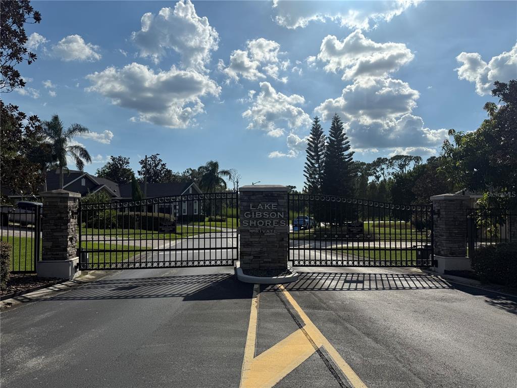 A gated entrance with stone pillars and a sign reading Lake Gibson Shores — ISLAND SHORES LANE, LAKELAND, FL
