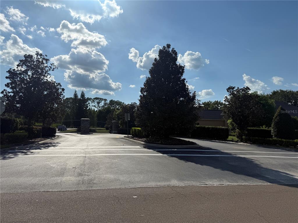 The entrance to a gated community features a paved road, landscaping, and a security gate — ISLAND SHORES LANE, LAKELAND, FL