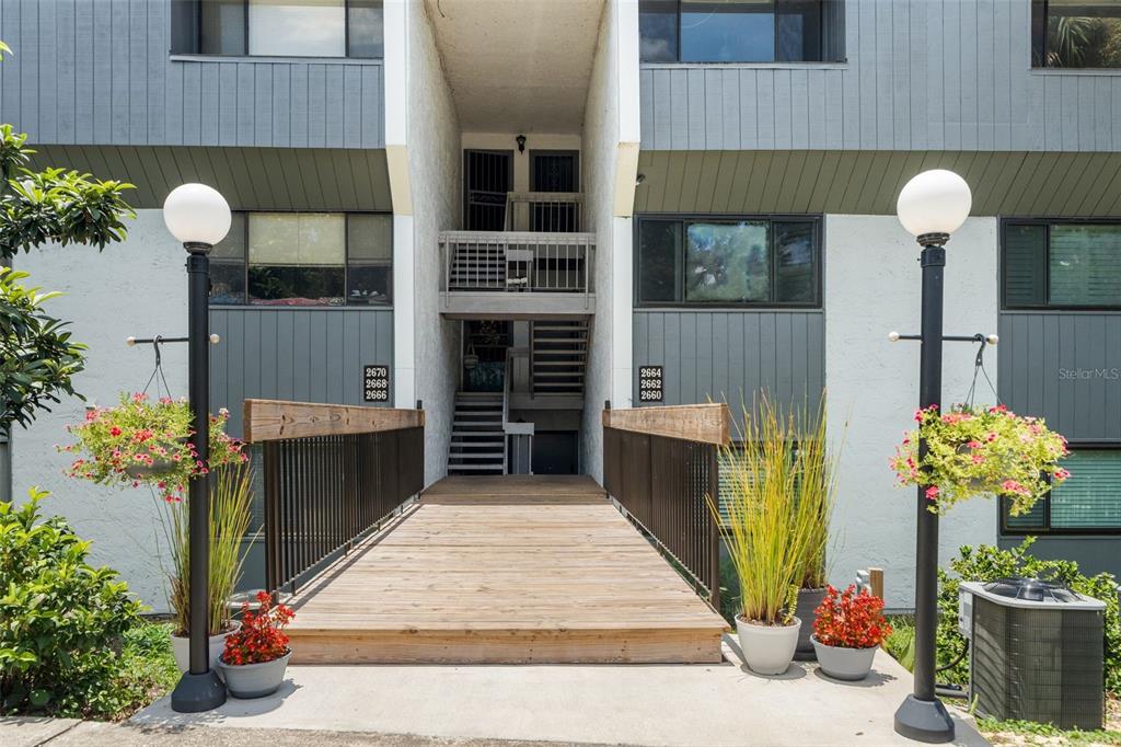 A wooden bridge leads to the entrance of a multi-story apartment building with gray siding — 2660 SW 14TH DRIVE UNIT 125, GAINESVILLE, FL