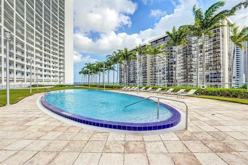 An oval swimming pool sits on a tiled patio surrounded by palm trees and buildings — 601 NE 36th Street # 2806, Miami FL 33137, MIAMI, FL