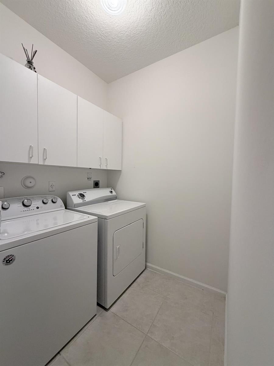A laundry room features white cabinets above a side-by-side washer and dryer on tile flooring — 6560 Villa Sonrisa Drive # 1321, Boca Raton FL 33433, BOCA RATON, FL