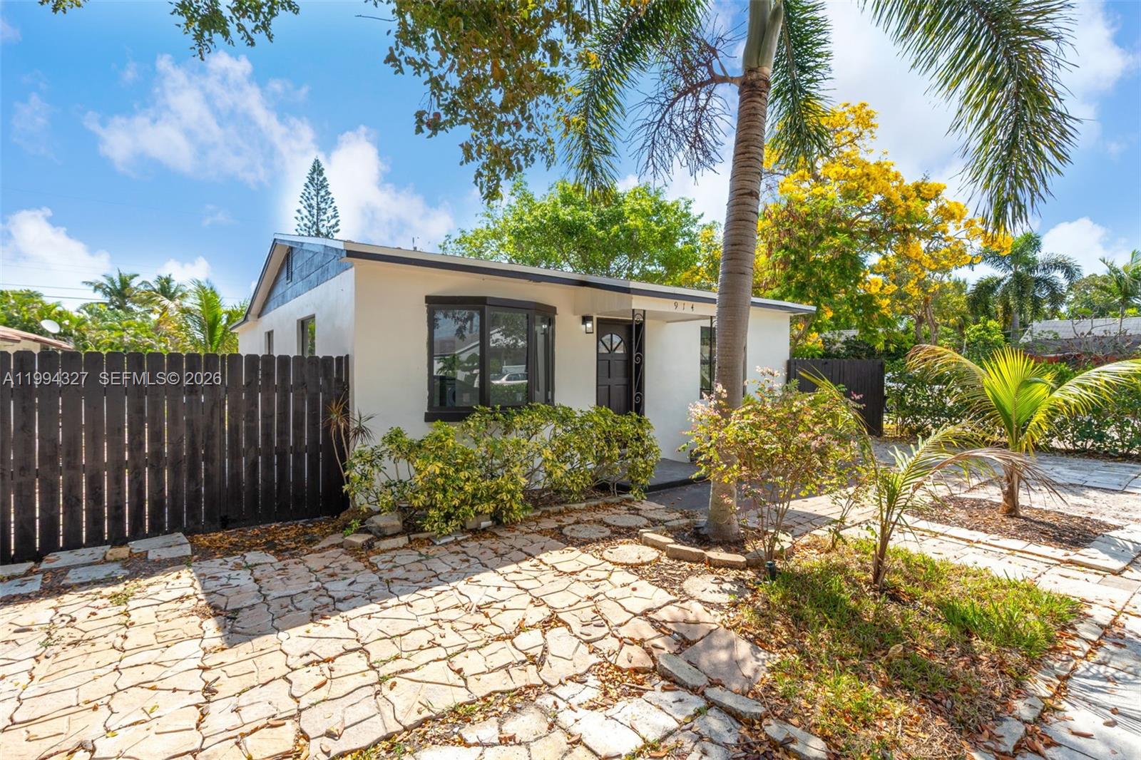 A single-story house with a stone patio, dark wooden fence, and palm tree in front — 914 S L St, Lake Worth FL 33460, LAKE WORTH, FL
