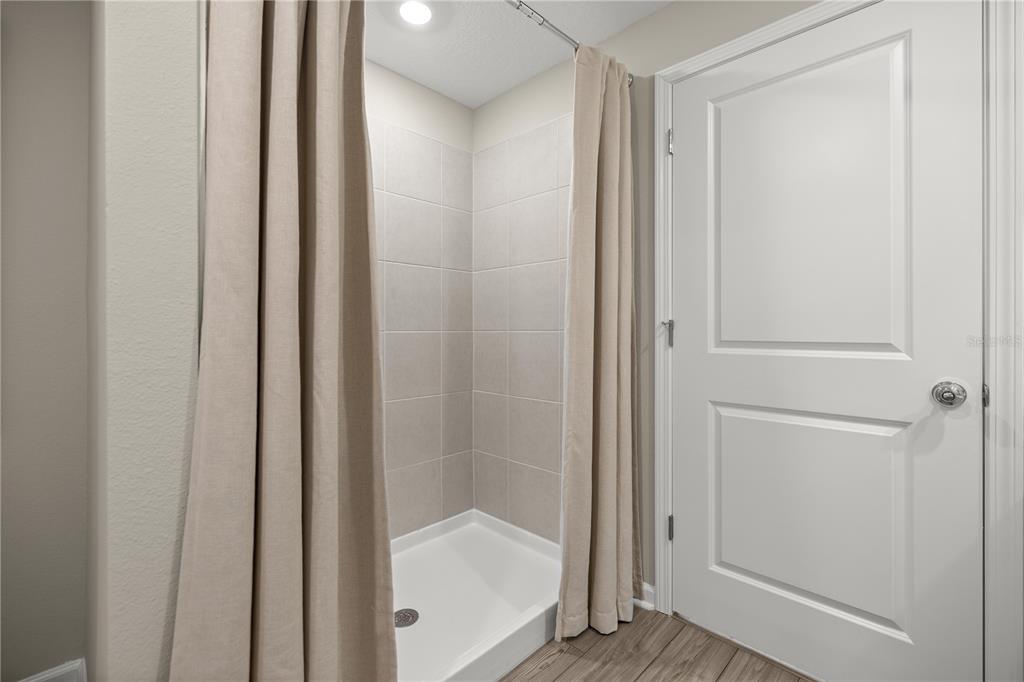 A walk-in shower with beige tile walls and a curtain stands beside a white door — 4239 SW 82ND LANE, OCALA, FL
