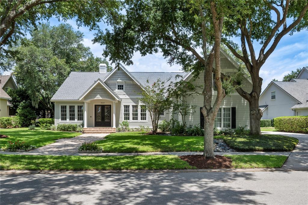 A light-colored house with a gabled roof and a front walkway sits behind large trees — 6241 BLAKEFORD DRIVE, WINDERMERE, FL