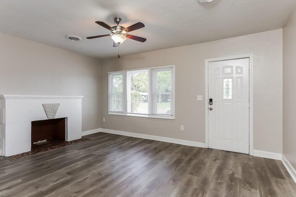 A living room with gray wood-look flooring, a white fireplace, and a white front door — FL