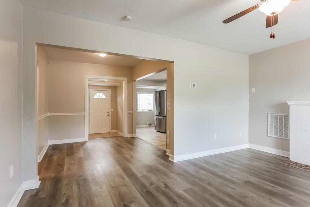 A living room with light gray walls, wood-look flooring, and an open doorway to a kitchen — FL