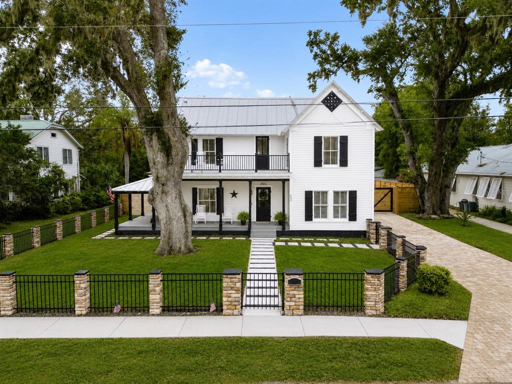 A two-story white farmhouse with black shutters and a metal roof sits behind a fence — 532 FAULKNER STREET, NEW SMYRNA BEACH, FL
