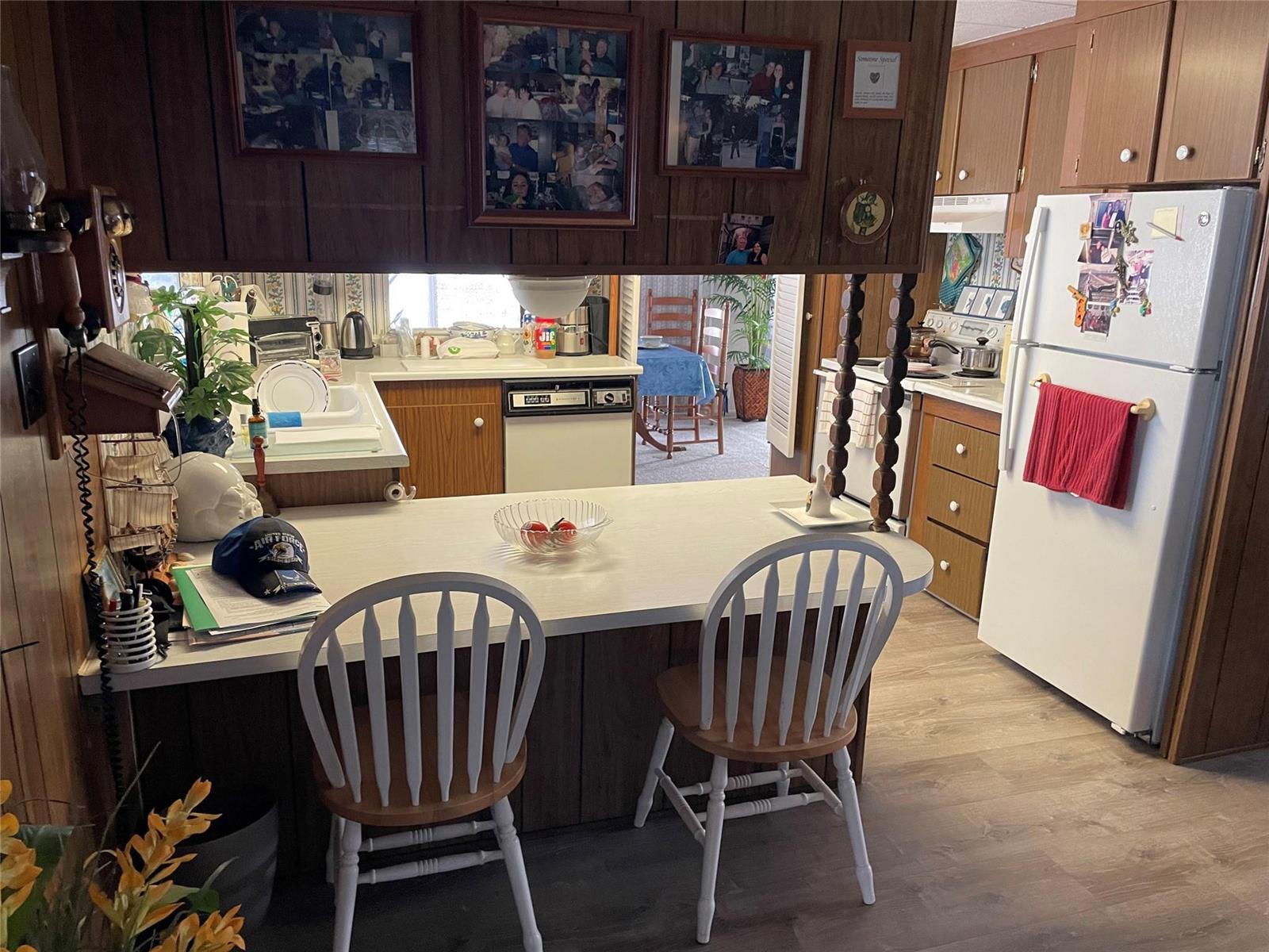 A kitchen features wood-paneled cabinets, a white breakfast bar with two chairs, and white appliances — 8621 SW 18th Court, Davie FL 33324, DAVIE, FL