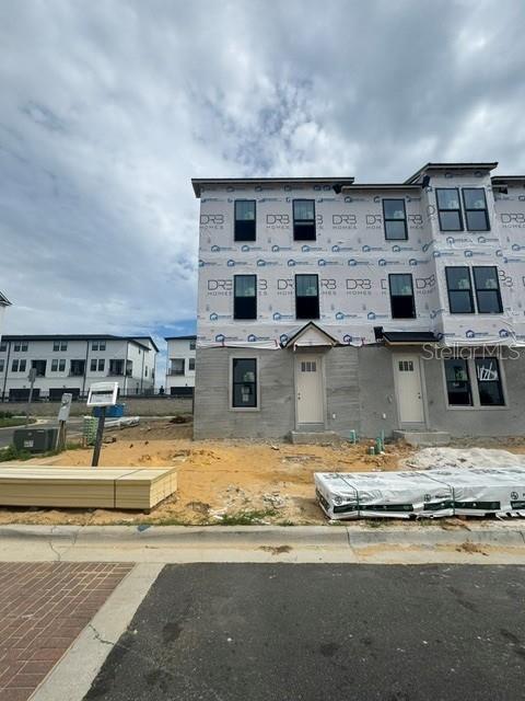 A three-story townhome under construction features a house wrap exterior and stacks of building materials — 15153 GROVESIDE ROAD, WINTER GARDEN, FL