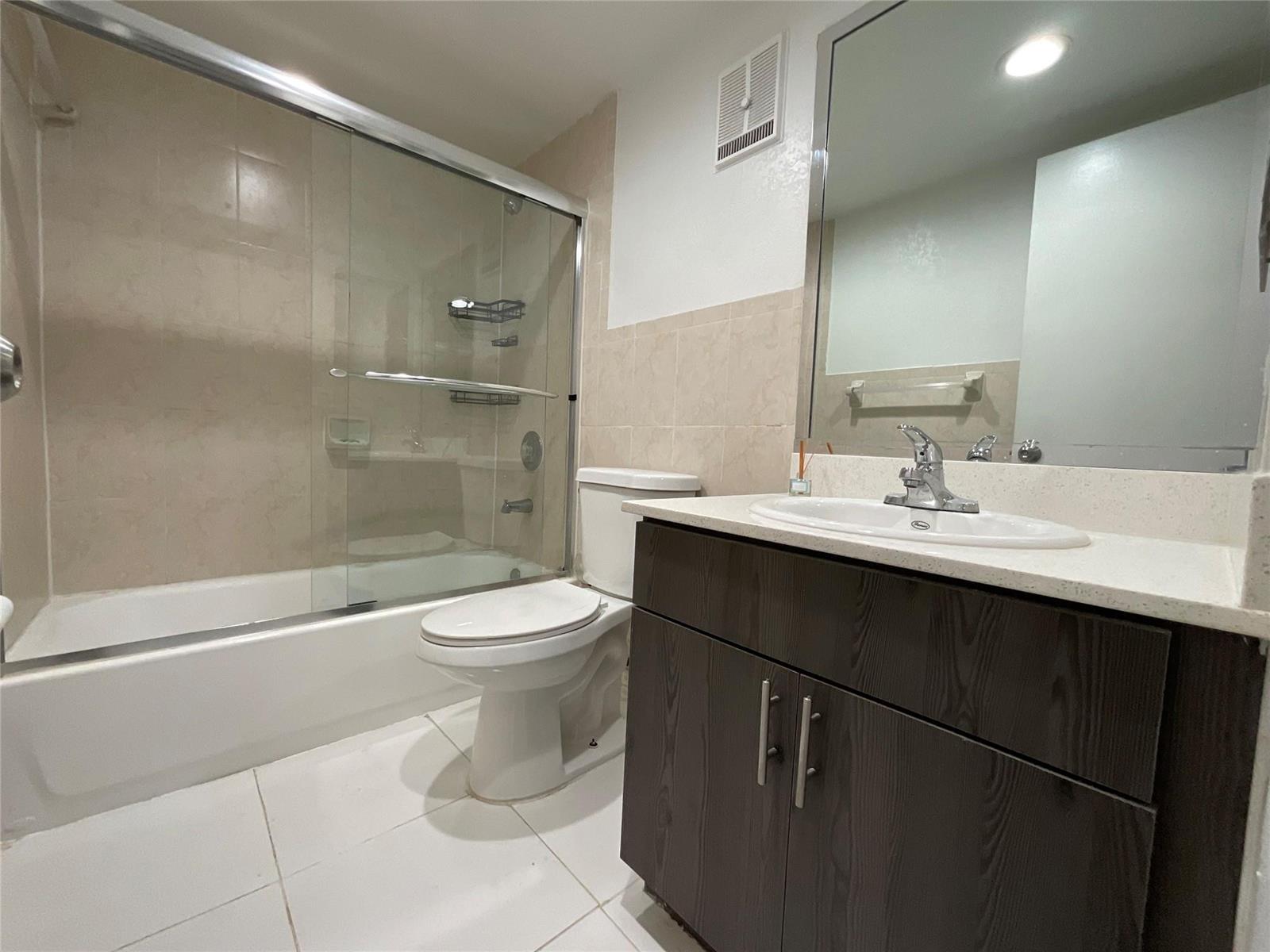 A bathroom features a glass-enclosed shower, a white toilet, and a dark wood vanity — 18335 NW 68 Avenue # 516, Hialeah FL 33015, HIALEAH, FL