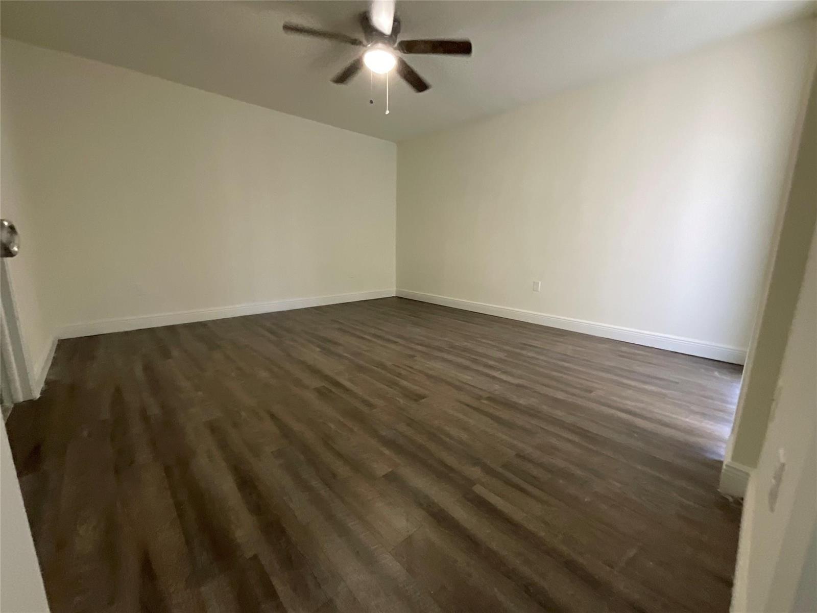 An empty room features white walls, dark wood-look flooring, and a ceiling fan — 18335 NW 68 Avenue # 516, Hialeah FL 33015, HIALEAH, FL