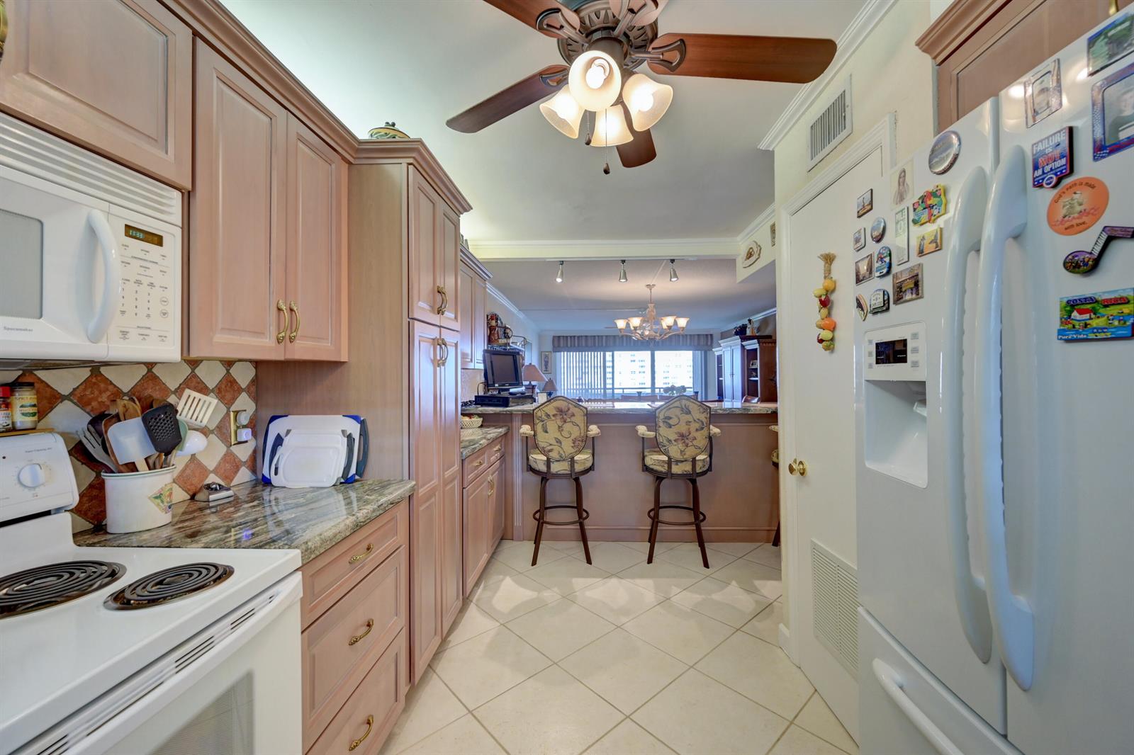A kitchen with light wood cabinets, granite countertops, and a breakfast bar overlooking the living area — 401 Briny Avenue # 708, Pompano Beach FL 33062, POMPANO BEACH, FL