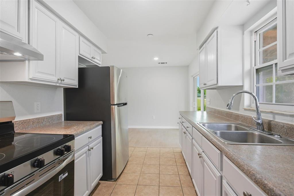 A galley kitchen features white cabinets, stainless steel appliances, laminate countertops, and tile flooring — 322 LITTLE ROCK COURT, OCOEE, FL