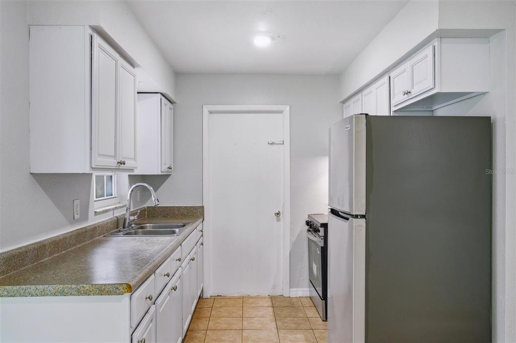 A kitchen features white cabinets, a stainless steel refrigerator, a sink, and tile flooring — 322 LITTLE ROCK COURT, OCOEE, FL