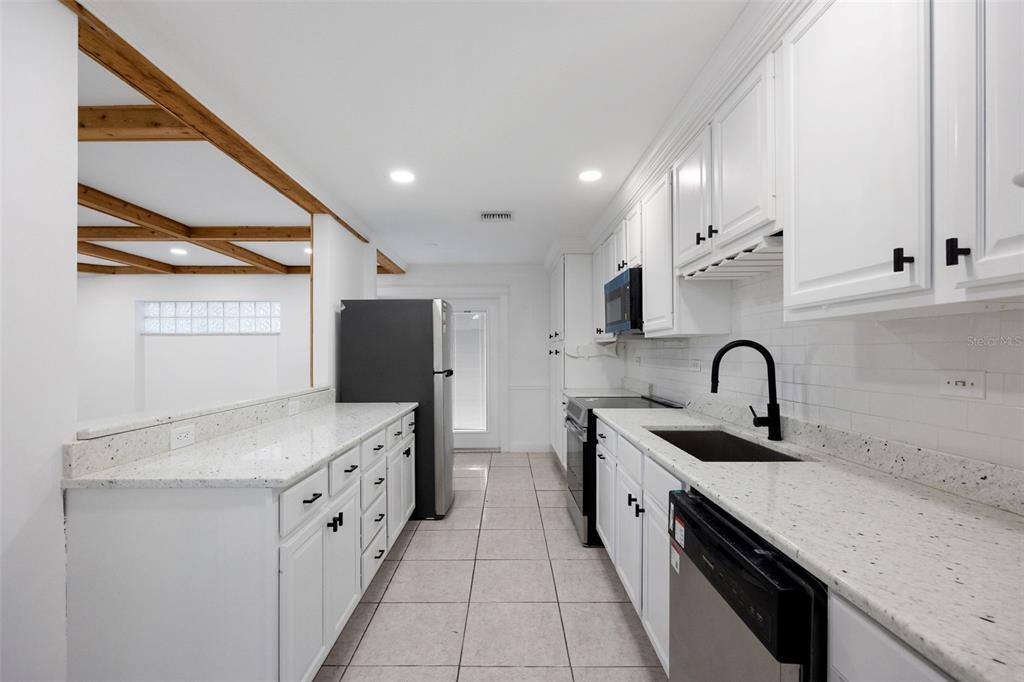 A galley kitchen features white cabinets, speckled countertops, a black faucet, and tile flooring — 1010 CLEARMONT STREET, SEBASTIAN, FL