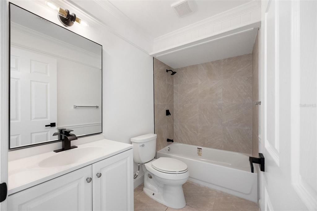 A bathroom features a white vanity, a toilet, and a bathtub with beige tiled walls — 1010 CLEARMONT STREET, SEBASTIAN, FL