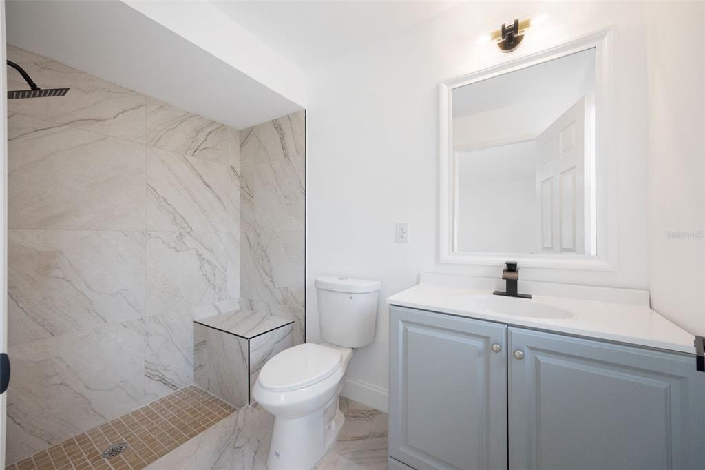 A bathroom features a walk-in shower with a built-in bench, a toilet, and a vanity — 1010 CLEARMONT STREET, SEBASTIAN, FL