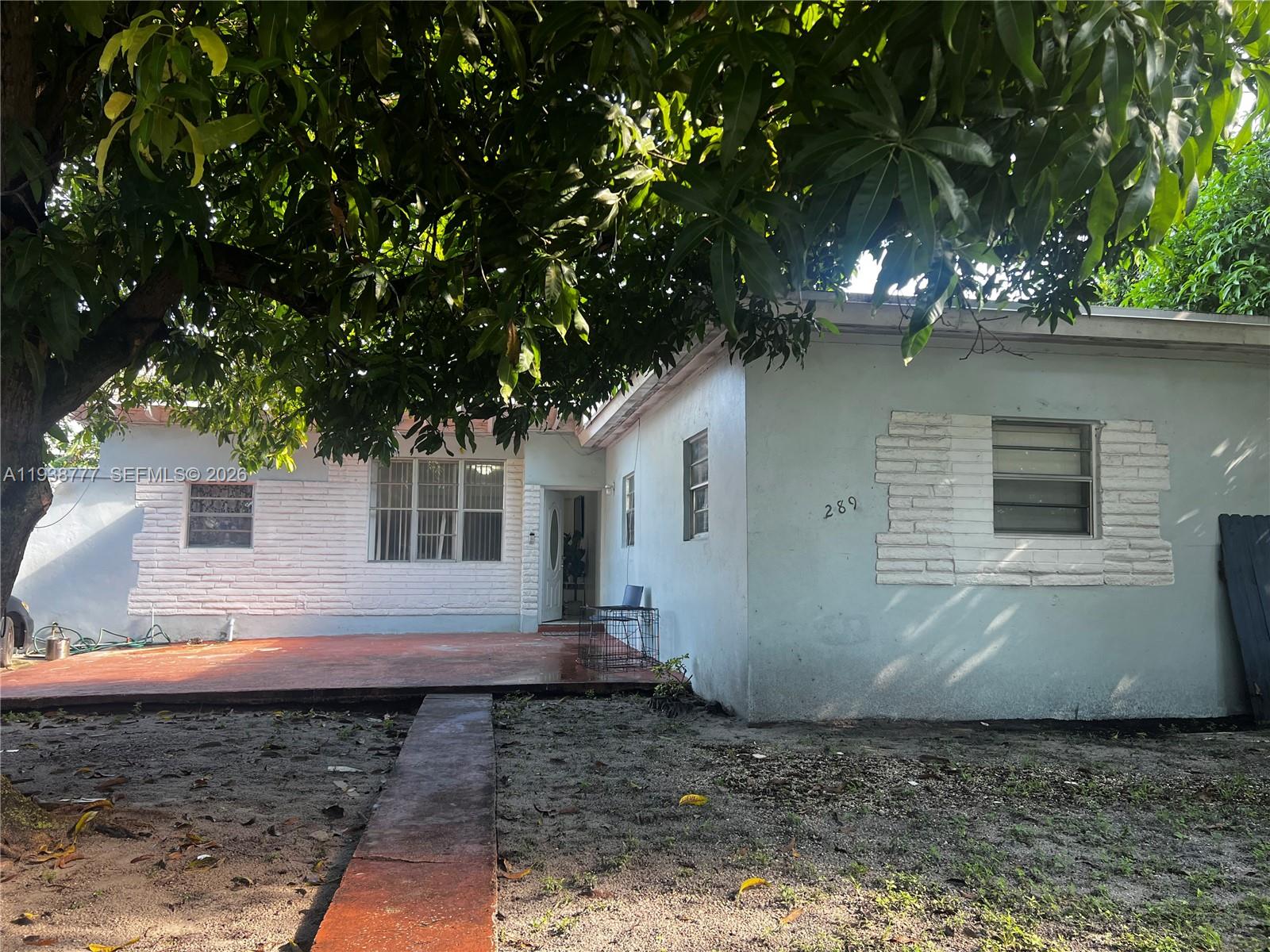The exterior of a light blue house features a brick-accented wall and a concrete patio — 289 NW 109th St, Miami FL 33168, MIAMI, FL