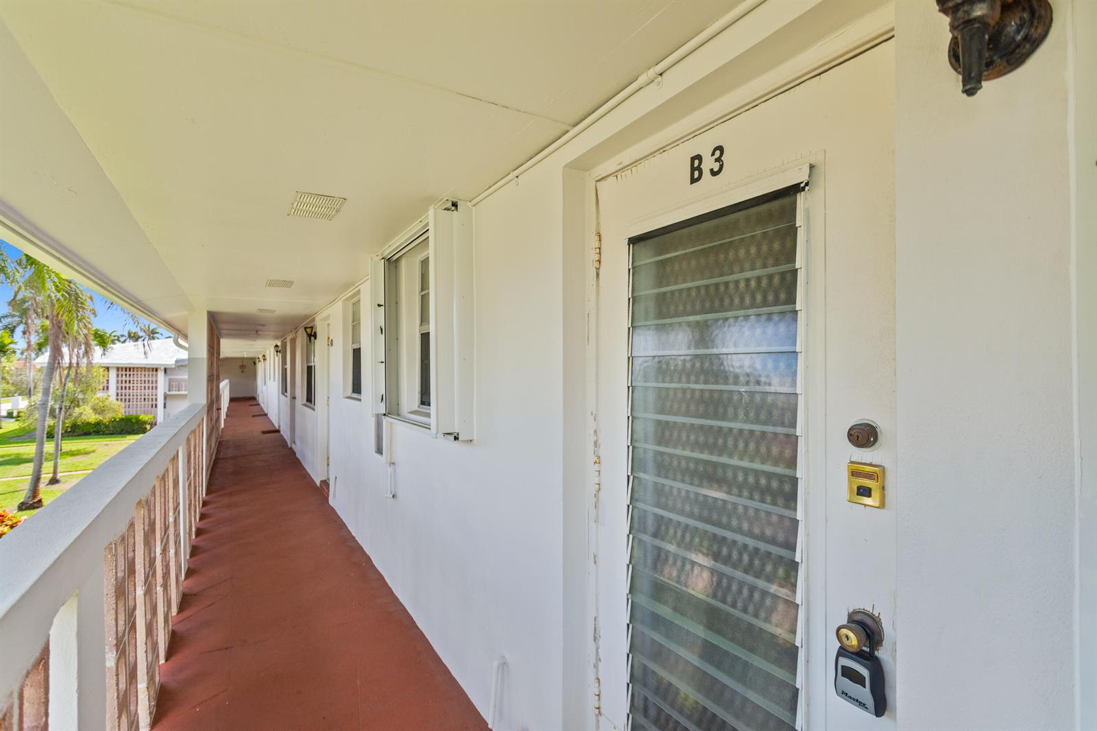 An outdoor apartment walkway features white walls, a louvered door labeled B3, and railings — 30 SE 13th Street # B3, Boca Raton FL 33432, BOCA RATON, FL