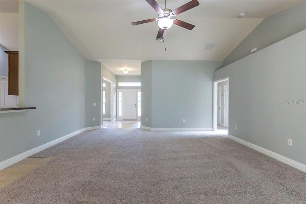 A spacious living room features light blue walls, beige carpeting, and a ceiling fan — 3401 EVERETT TERRACE, NORTH PORT, FL