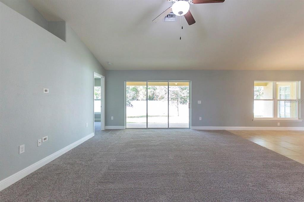 A spacious living room features gray carpet, light gray walls, a ceiling fan, and sliding doors — 3401 EVERETT TERRACE, NORTH PORT, FL